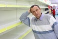 Elderly man leans against empty shelves