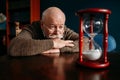 Elderly man looking on sandglass in home office