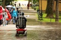 An elderly man in a mechanical wheelchair is passing by the alee of the park past a passing group of children. Sympathy and help