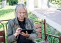 Elderly man opens application on smartphone while sitting on bench in city park Royalty Free Stock Photo