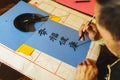 Elderly man painting brush and black ink Japanese characters on blue paper. Royalty Free Stock Photo