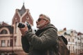 An elderly man photographs city sights. Mature tourist, photography as a hobby. In a jacket, winter weather