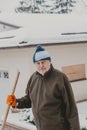 Elderly man with plastic shovel stands in snowy yard