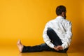 Elderly man practices yoga in formal office clothes. on a yellow background.