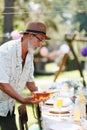 Elderly man preparing refreshments for a summer garden party, pouring wine in glass.