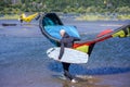 An elderly man in a protective suit with a sail and a windsurf board walks on the water of the Columbia River in Hood River to the