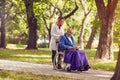 Elderly man reading book in wheelchair with nurse in the park Royalty Free Stock Photo