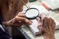 Elderly man reading writings in a notebook with magnifying glass near the window at home Royalty Free Stock Photo