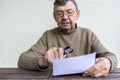 Elderly man reads fine print on white piece of paper using magnifying glass. Magnifier helps old senior Royalty Free Stock Photo