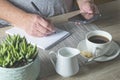 Elderly man seated at table, holding mobile phone and writing in note book, with cup of coffee Royalty Free Stock Photo