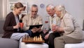 Elderly man showing friends new project on tablet pc, chess play brake, fun