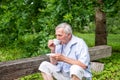 Elderly man sipping tea on a wooden bench in a leafy garden, enjoying the tranquil pleasures of nature, quiet and