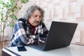 An elderly man sits at a table and watches a video on a computer. Senior man working on laptop at home Royalty Free Stock Photo