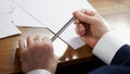 Elderly man sits at a table with white sheets of paper and holds a metal pen in his wrinkled hands. Concept of writing a will or Royalty Free Stock Photo