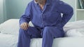 Elderly man sitting on bed edge, stretching and having sudden lower back pain