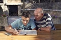 A elderly man sitting doing crosswords hobby with his grandson