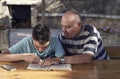 A elderly man sitting doing crosswords hobby with his grandson