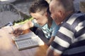 A elderly man sitting doing crosswords hobby with his grandson