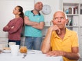 Elderly man sitting at table, unhappy family couple quarrelling