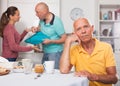 Elderly man sitting at table, unhappy family couple quarrelling