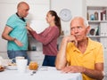 Elderly man sitting at table, unhappy family couple quarrelling