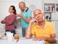 Elderly man sitting at table, unhappy family couple quarrelling