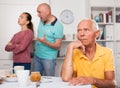 Elderly man sitting at table, unhappy family couple quarrelling