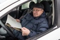 An elderly man is sitting at the wheel of a car. The pensioner r