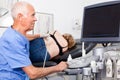 Elderly man sonographer using ultrasonography machine checking female patient in hospital diagnostic room