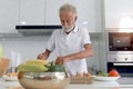 Elderly man standing at kitchen counter with colorful fresh vegetables, fruits and food ingredients, senior man preparing for Royalty Free Stock Photo