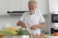 Elderly man standing at kitchen counter with colorful fresh vegetables, fruits and food ingredients, senior man preparing for Royalty Free Stock Photo