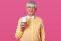 Elderly man stands with coffe against pink wall. Senior holds big cup ready for drinking hot baverage. Grey haired male with Royalty Free Stock Photo