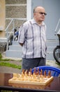 Elderly man stands near the chess table waiting for his opponent in amateur competitions