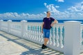 An elderly man stands near a white fence with balusters and looks at the blue sea Royalty Free Stock Photo