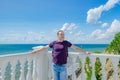 An elderly man stands near a white fence with balusters and looks at the blue sea Royalty Free Stock Photo