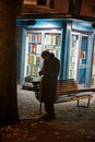 An elderly man strolls in front of a kiosk of used books during