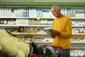 Elderly man at the supermarket shopping with a grocery list and pushing cart. Retail concept Royalty Free Stock Photo