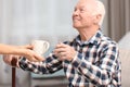 Elderly man taking cup of tea from female caregiver Royalty Free Stock Photo