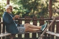 An elderly man is typing a message on the phone while relaxing on a bench. Active lifestyle in old age. Spending time in the fresh