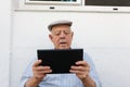 Elderly man is using a tablet in the yard of his house