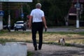 An elderly man walks with a dog on the road