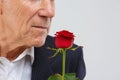 An elderly man on a white background, in a black smart suit, stands with one rose in his hand. Royalty Free Stock Photo