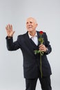 An elderly man on a white background wearing a black smart suit is waiting for someone with a rose in his hand Royalty Free Stock Photo