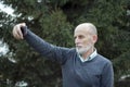 An elderly man with a white beard and bald head makes a selfie