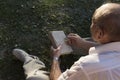 An elderly man in a white shirt is sitting on a blanket, on the ground in a park and reading an interesting book. A pensioner Royalty Free Stock Photo