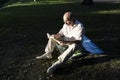 An elderly man in a white shirt is sitting on a blanket, on the ground in a park and reading an interesting book. A pensioner Royalty Free Stock Photo