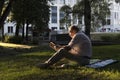 An elderly man in a white shirt is sitting on a blanket, on the ground in a park and reading an interesting book. A pensioner Royalty Free Stock Photo