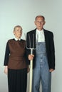 Elderly man and woman in art performance, replica of painting american gothic. Retro style, comparison of eras and