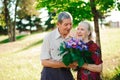 An elderly man of 80 years old gives flowers to his wife in a su