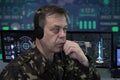 An elderly military man with headphones looks at the monitor against the background of a world map in the military center. Concept Royalty Free Stock Photo